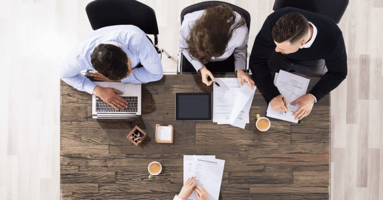 Three professionals sitting at a table reviewing a resume together during a meeting